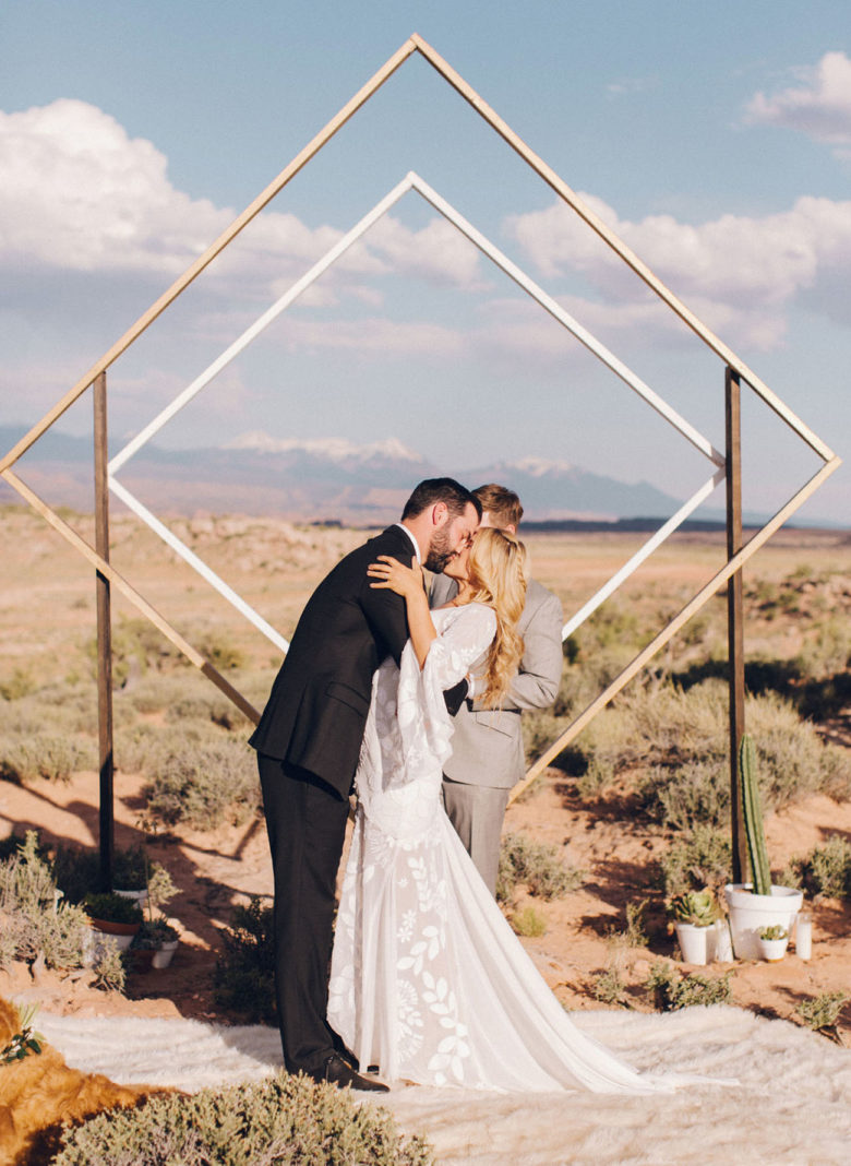 couple kiss in the desert in front of officiant and a concentric square diamond frame