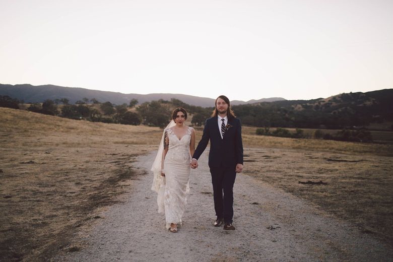 couple in wedding attire holding hands on a country road
