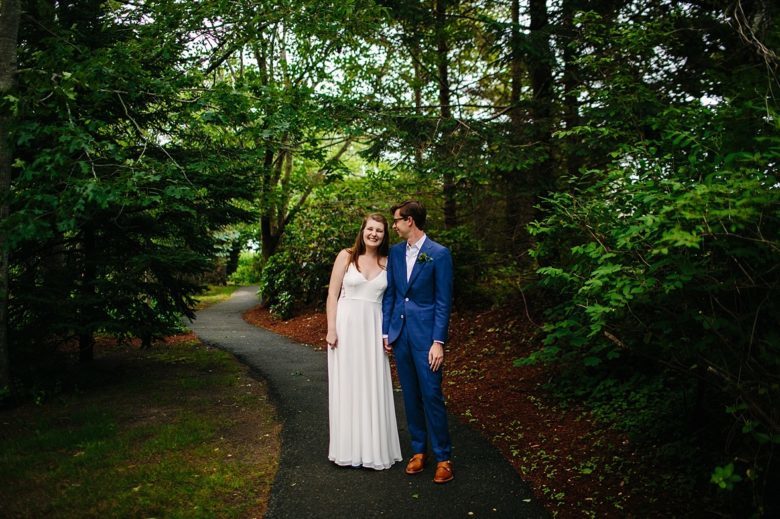 couple in wedding attire stand on small paved path in a wooded park