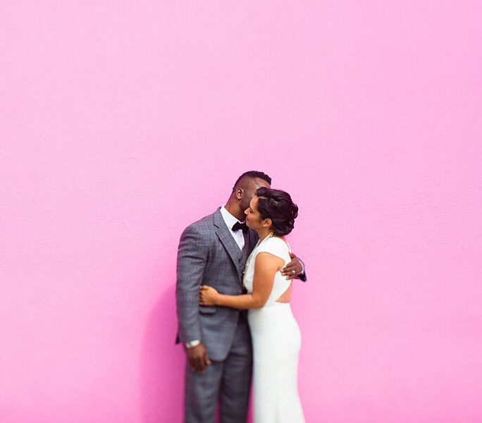 wedding couple standing in front of a pink wall