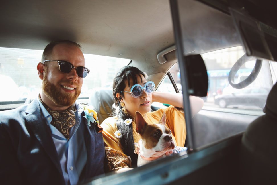 Stylishly hip couple in back seat of taxi wearing sunglasses, holding dog