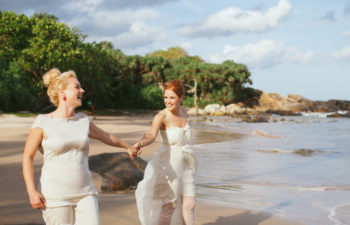 Two brides holding hands on a beach