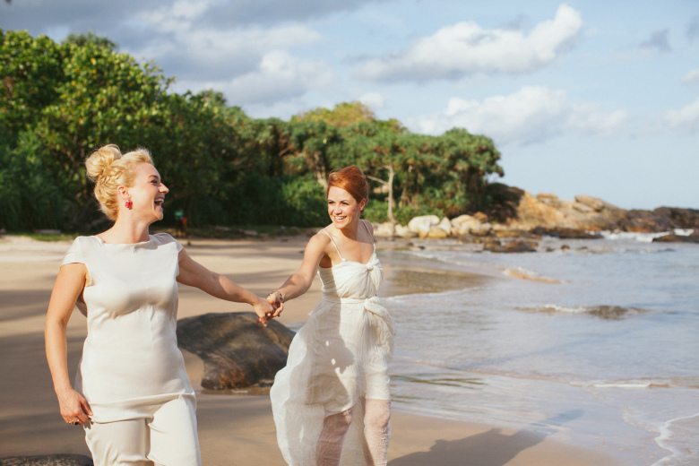 Two brides holding hands on a beach