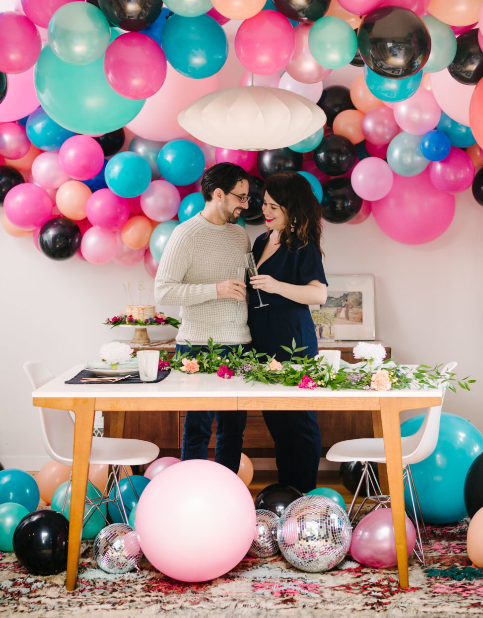 couple toasting with champagne flutes in a room filled with balloons and disco balls