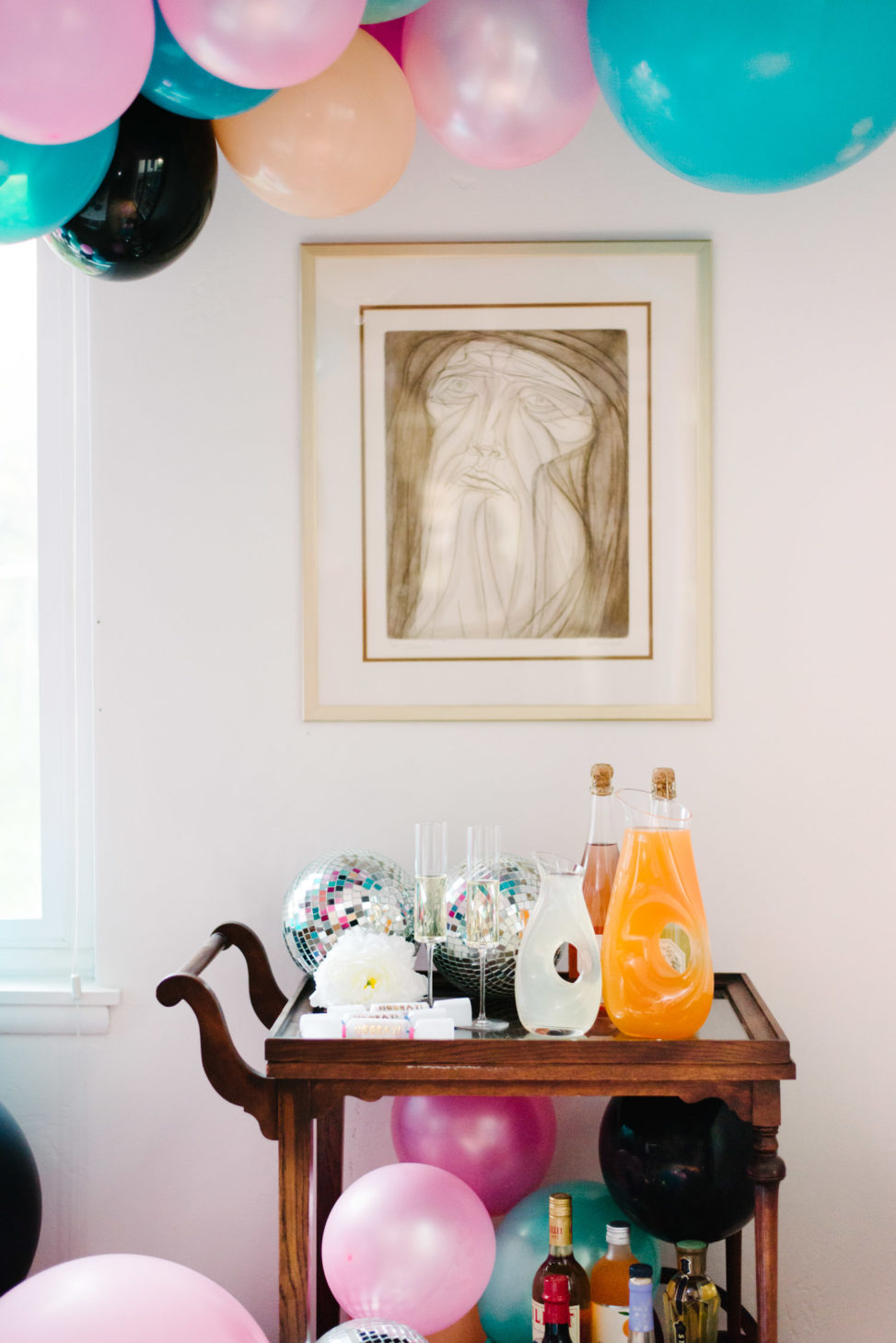 vintage bar cart covered in balloons and disco balls with orange juice and lemonade in crate and barrel pitchers with champagne flutes