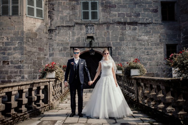 bride and groom holding hands on a bridge in front of castle