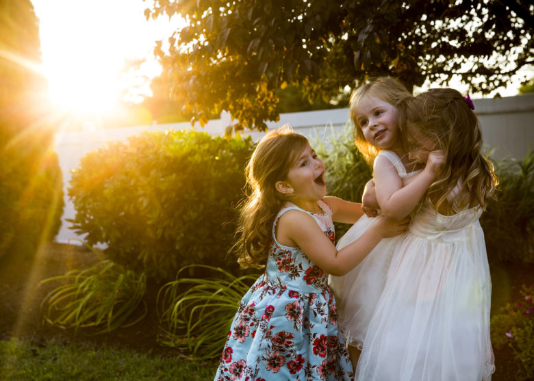 three little girls playing in a yard with a sun flare behind them