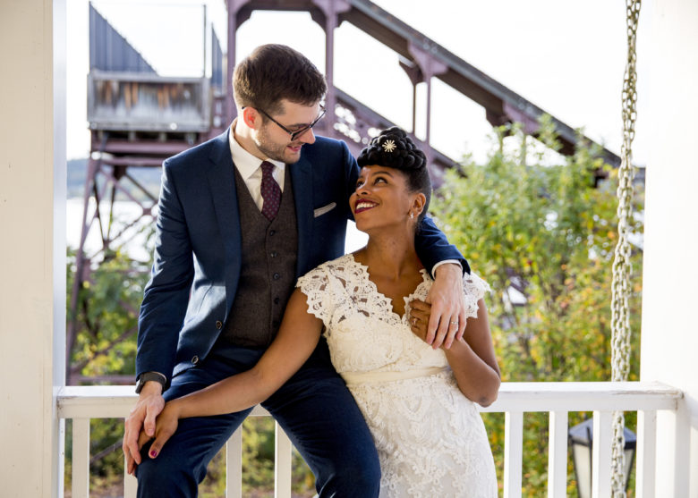 groom sitting on a porch railing with arm around bride looking up at him