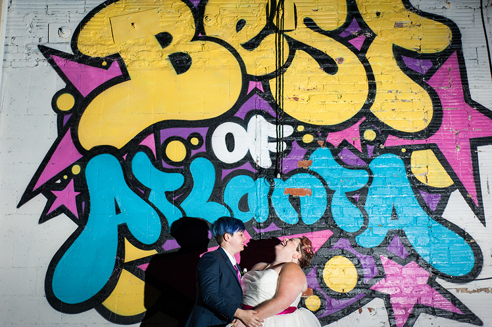 Queer wedding couple holding hands and laughing while standing in front of colorful "Best of Atlanta" mural