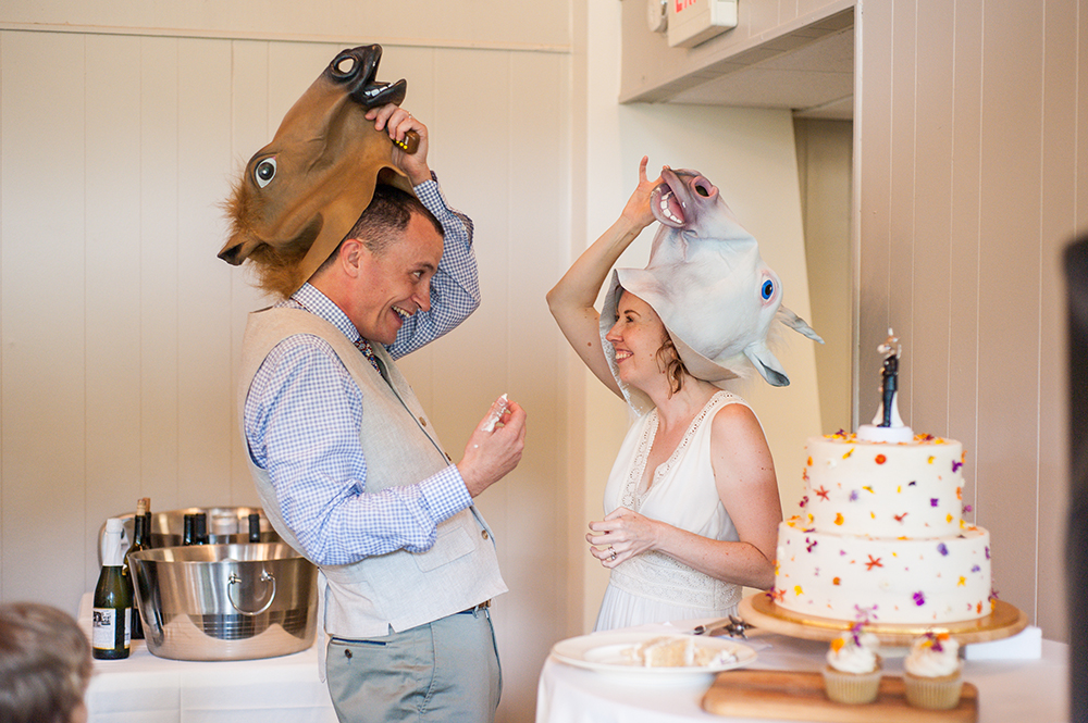 Bride and groom take off silly horse heads and grin at each other during their cake cutting in a photo by You Are Raven