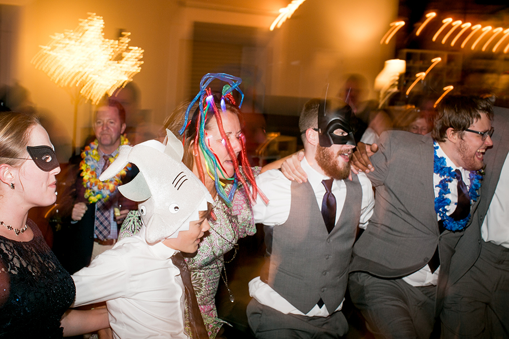Light-filled photo of wedding dance party with silly masks and hats in a photo by You Are Raven