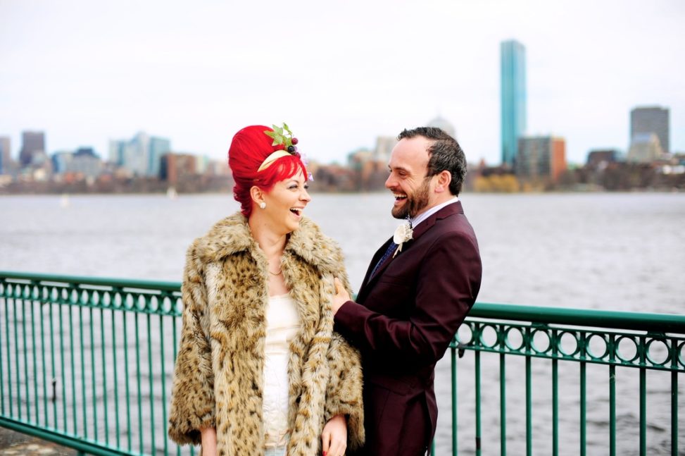 bride with red hair and leopard coat with groom in burgundy suit on waterfront