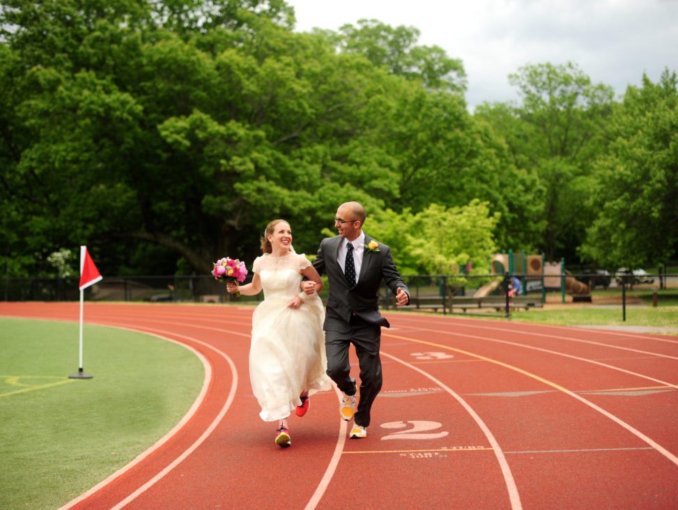 newlyweds running down a race track with linked arms