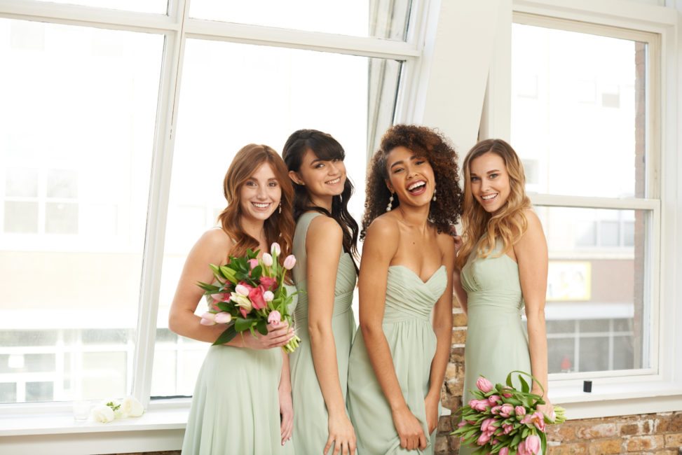 bridesmaids smiling in front of loft windows wearing light mint green dresses in different styles