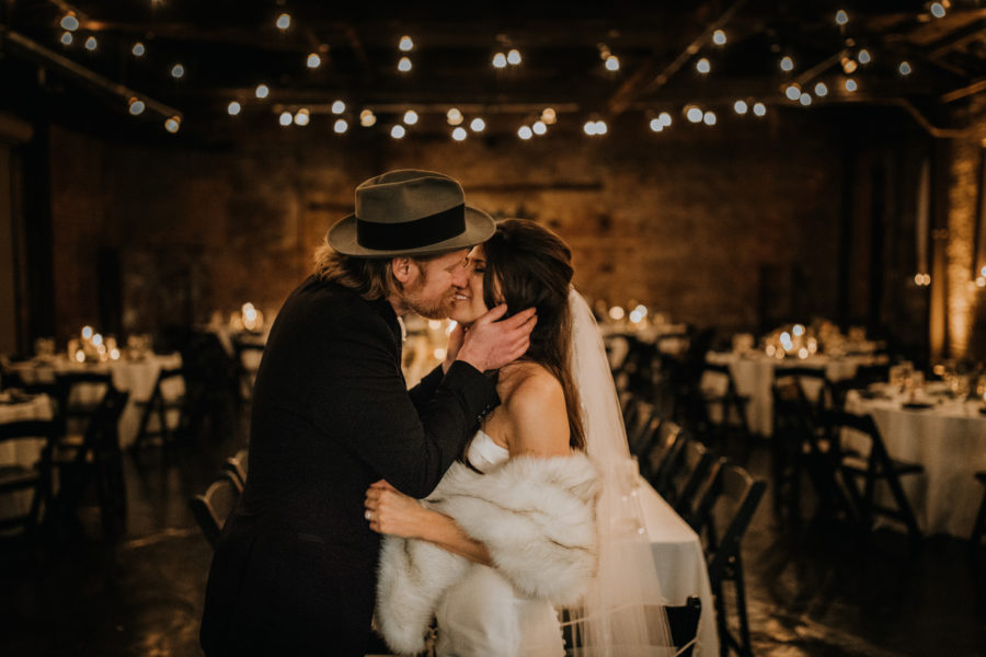 Couple kissing in dark reception hall with string lights overhead