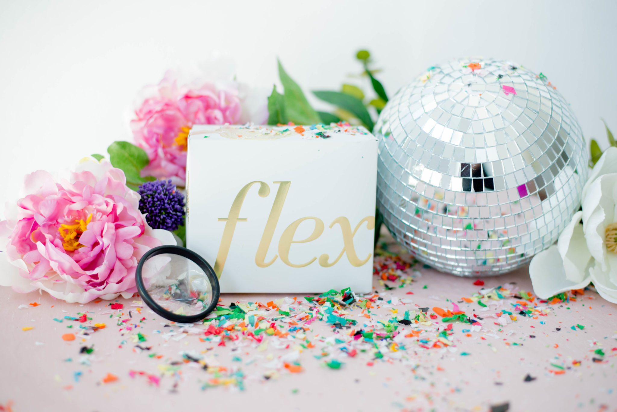 a flex menstrual disc in a pile of confetti next to a disco ball and flowers