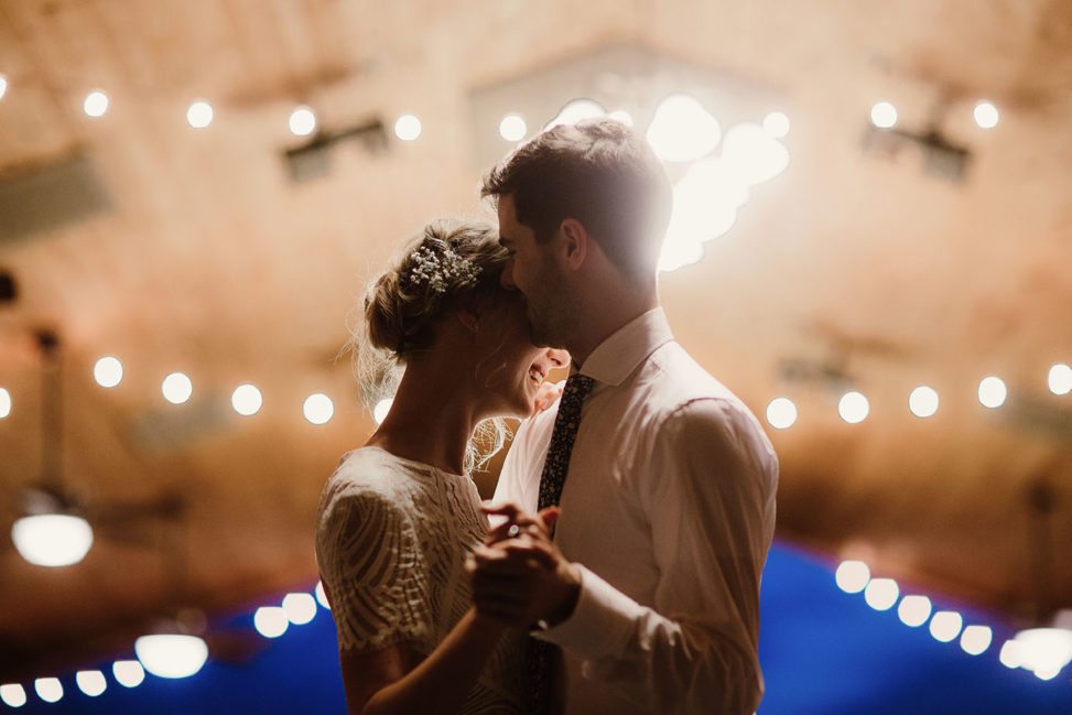 bride and groom dancing in a barn with string lights