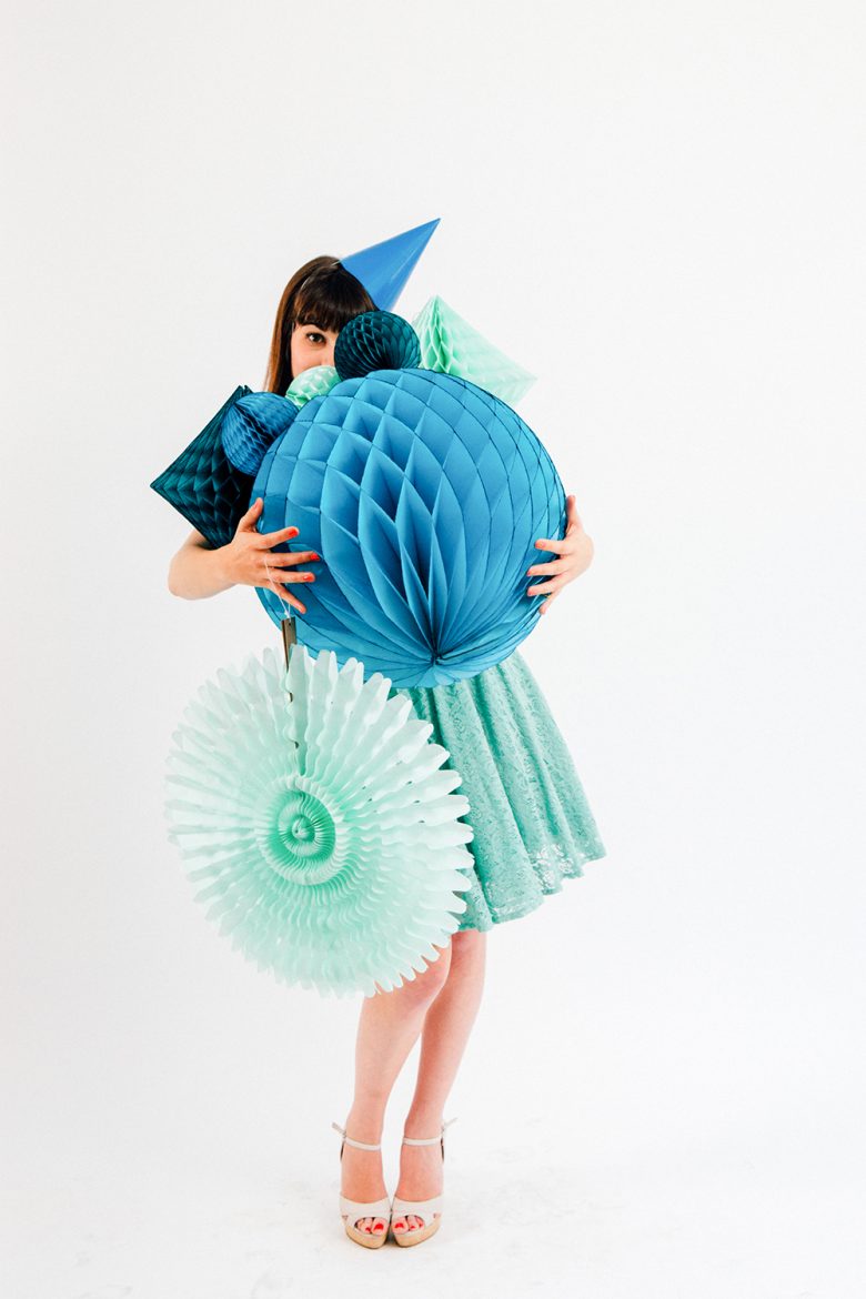 woman carrying blue tissue paper honeycomb balls and pinwheels wearing a blue party hat