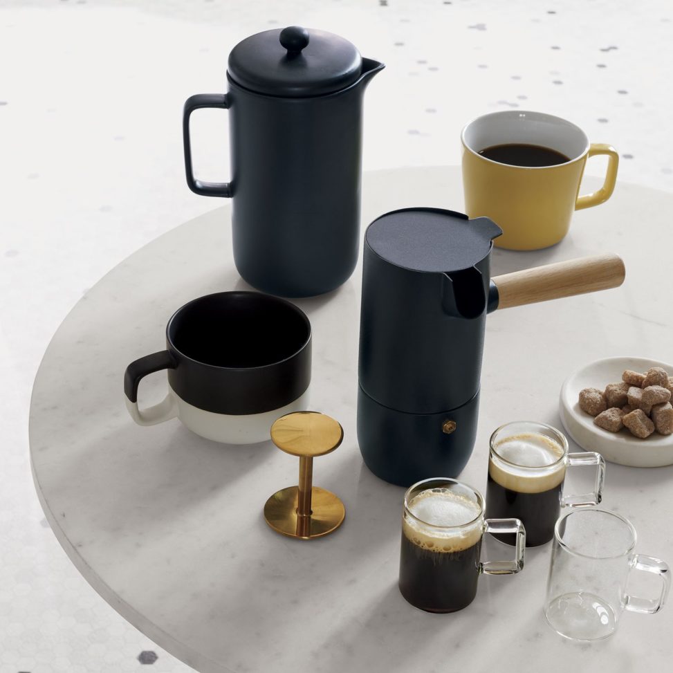 Black coffee pots next to coffee mugs on marble table