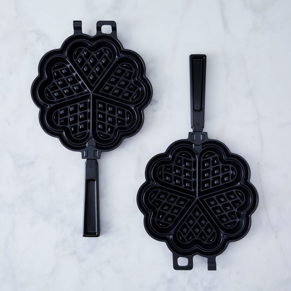 Two waffle irons with heart shapes on a marble table