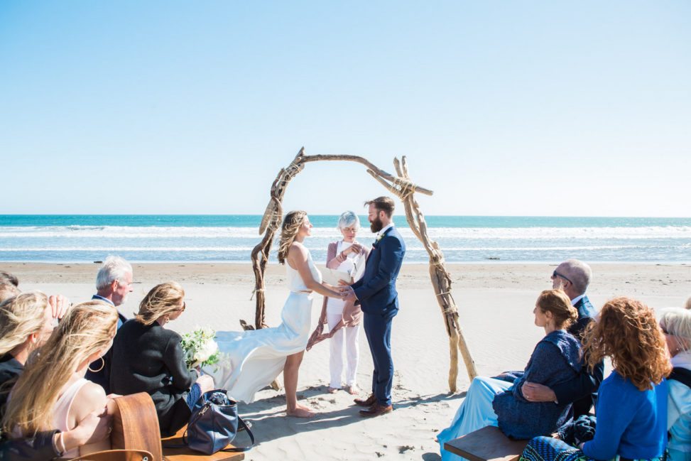wedding ceremony at a windy beach with a driftwood arch