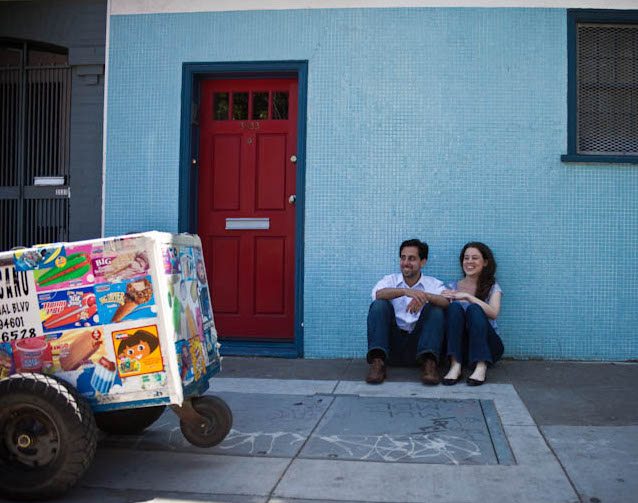 woman and her husband sitting in front of a light blue tiled wall next to an ice cream push cart
