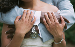 A close up image of a man standing behind a woman with his arms wrapped around her. Prenups.