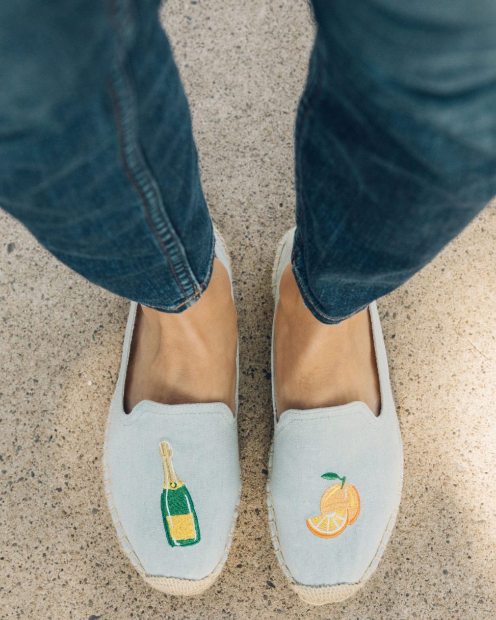 Blue slip-on shoes with a champagne bottle and orange embroidered design
