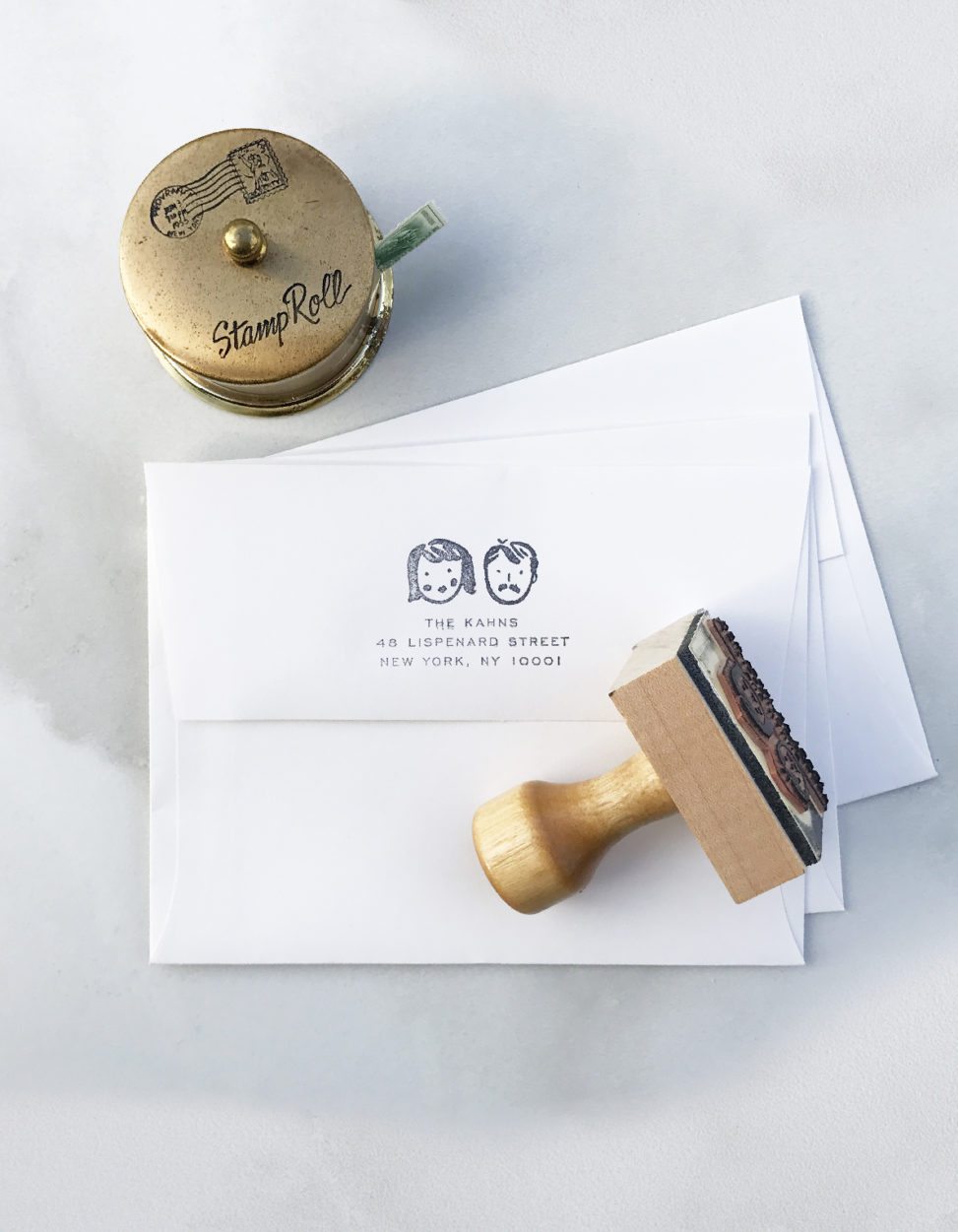 Address stamp with illustrated portraits, envelope and stamp roll on marble table