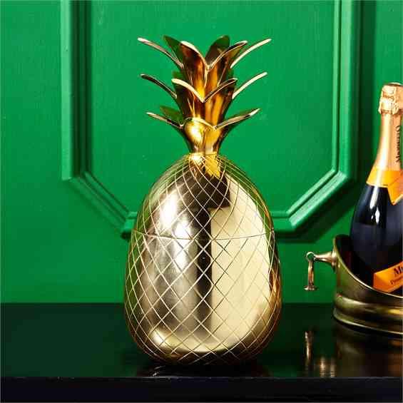 Pineapple shaped gold ice bucket with lid sitting on bar before green wall