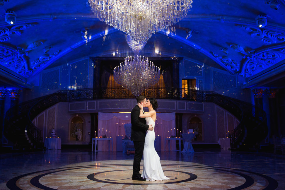 bride and groom kissing on purple lit dance floor under chandeliers