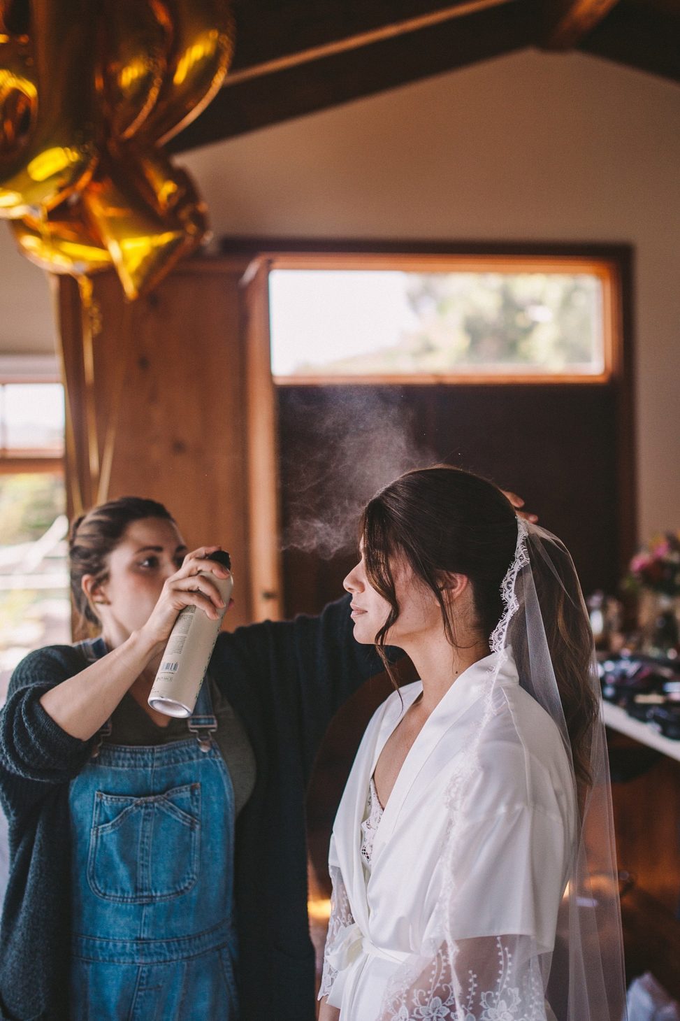 a hairstylist hairsprays a brunette bride's hair for her wedding hairstyle