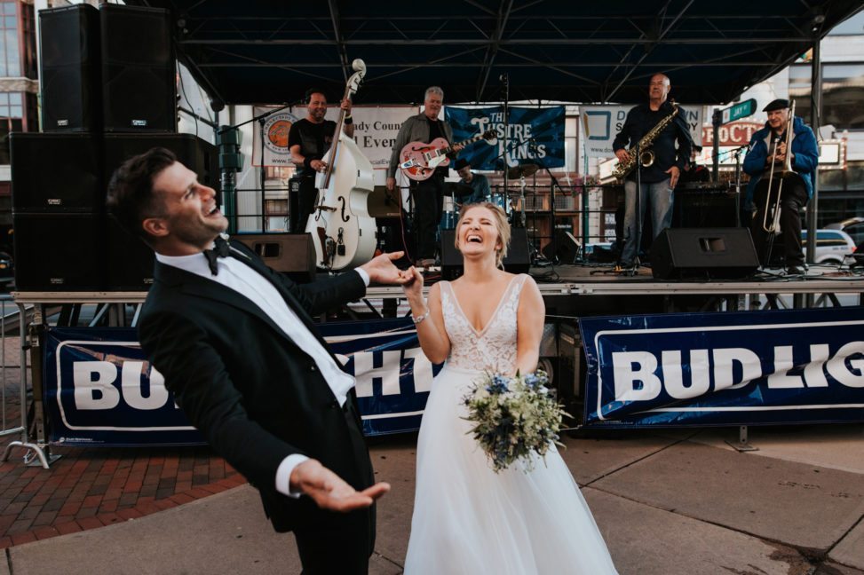 couple in a wedding dress and tuxedo dancing and laughing in front of Bud Light signs and a live band