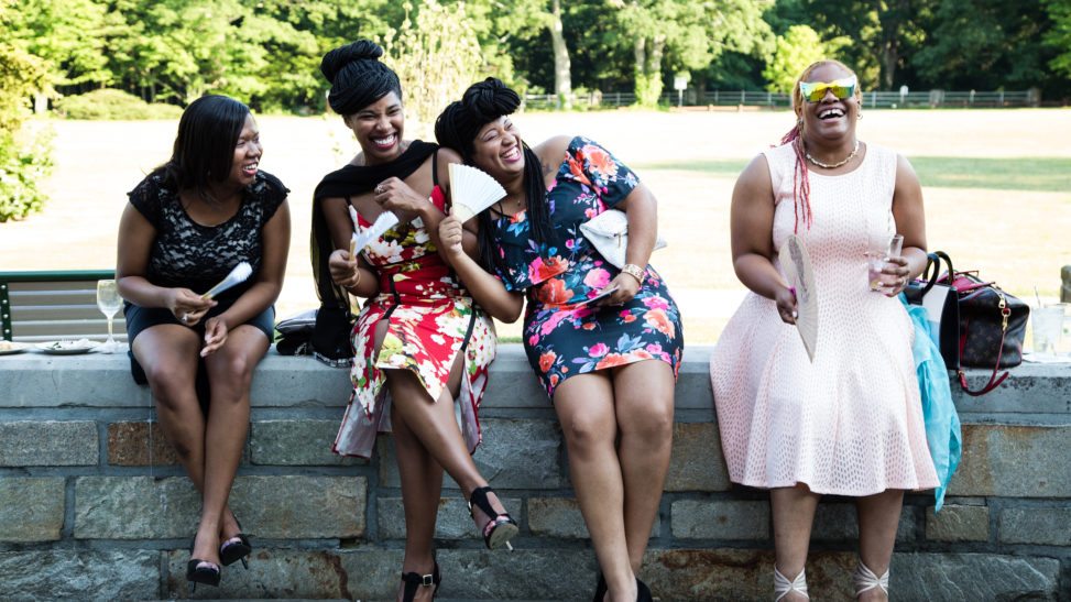 A group of wedding guests sit on a wall and laugh