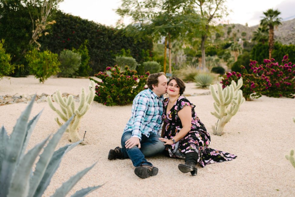 man kissing woman on the cheek while sitting between cacti 