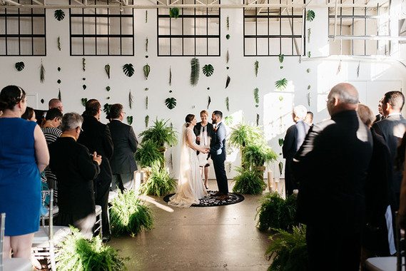 wedding ceremony in an industrial building with tropical leaves hanging as backdrop, and ferns everywhere 
