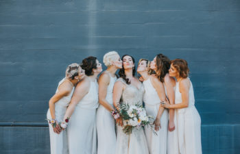 Bridesmaids in white kissing a bride