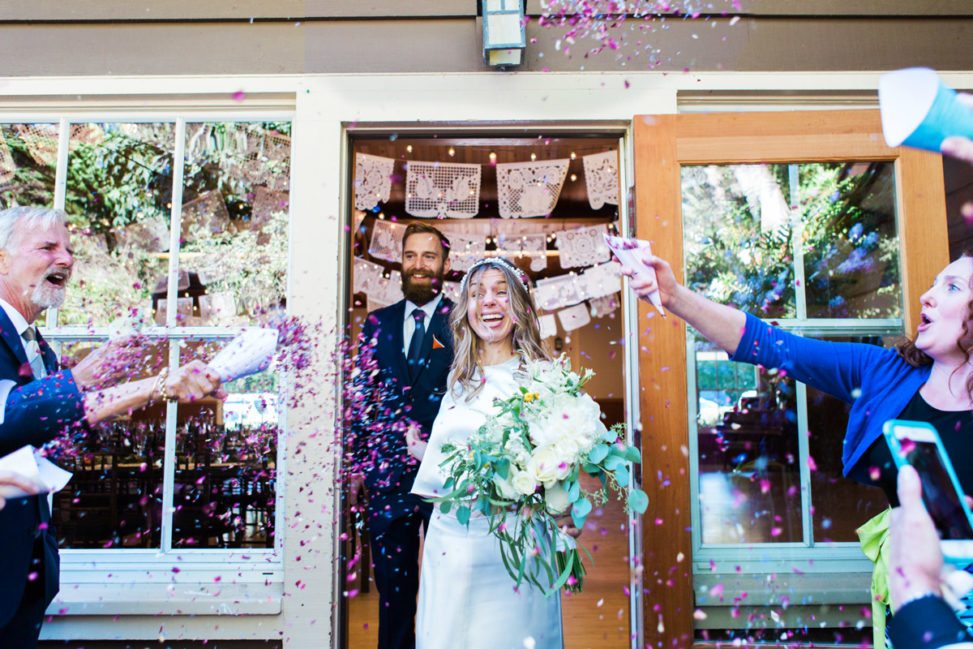 a smiling couple walking through a door being showered with confetti