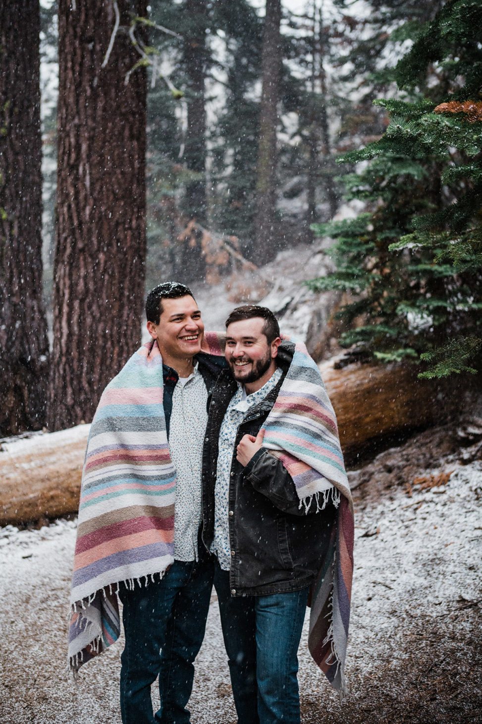 two men under a blanket in the snowy woods