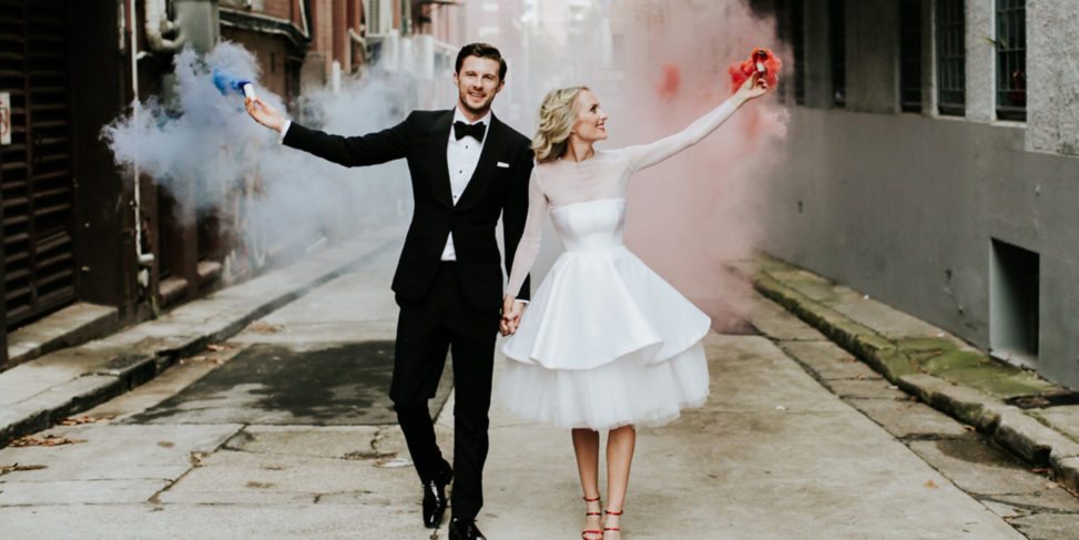 bride and groom holding hands and releasing red and blue smoke bombs