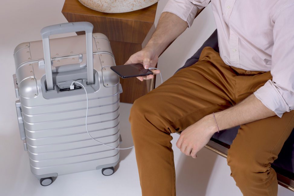 sitting man in brown pants charging phone on rolling luggage