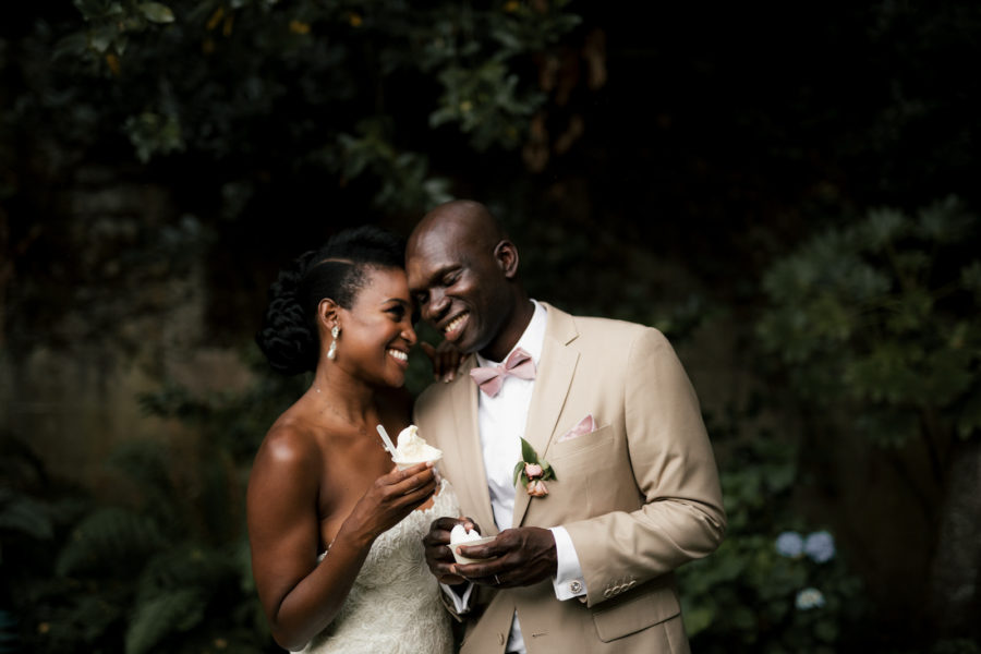 Couple in wedding clothes smiling at each other and eating ice cream