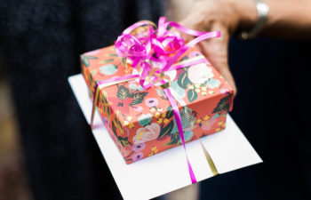 Small gift box wrapped in colorful floral paper tied with bright pink and gold ribbon to a card