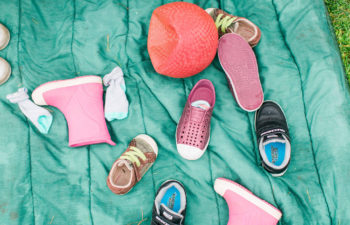 Several different sizes and styles of children's shoes strewn over a blanket outside