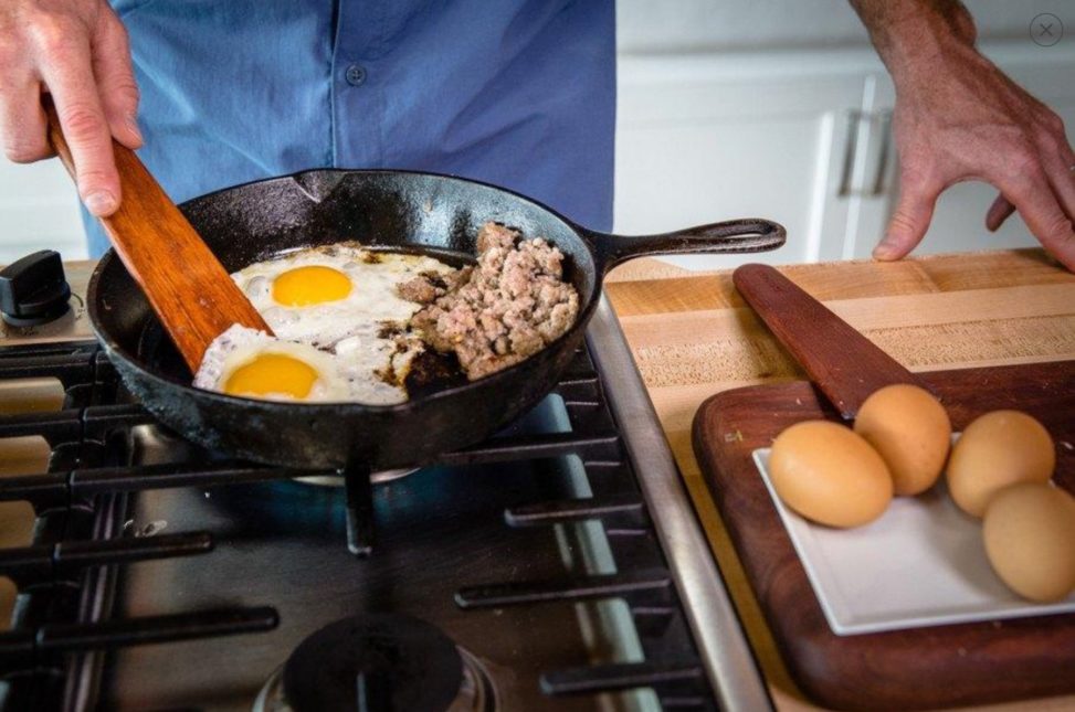 Person sauteing eggs on stove with wooden tools