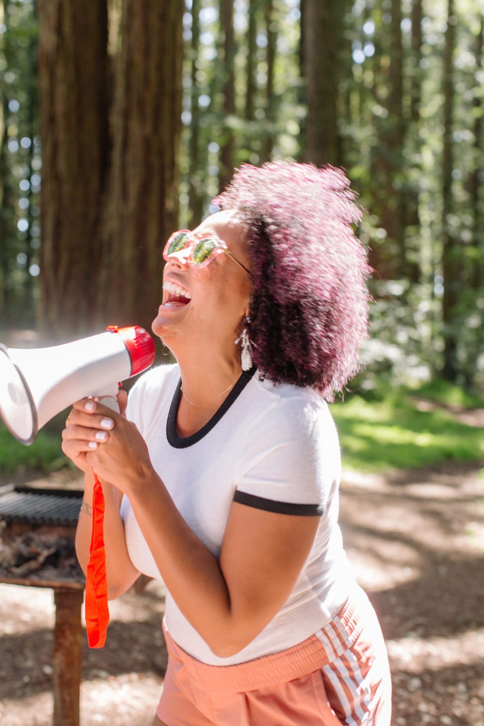 woman in the woods near a grill holding a megaphone and laughing