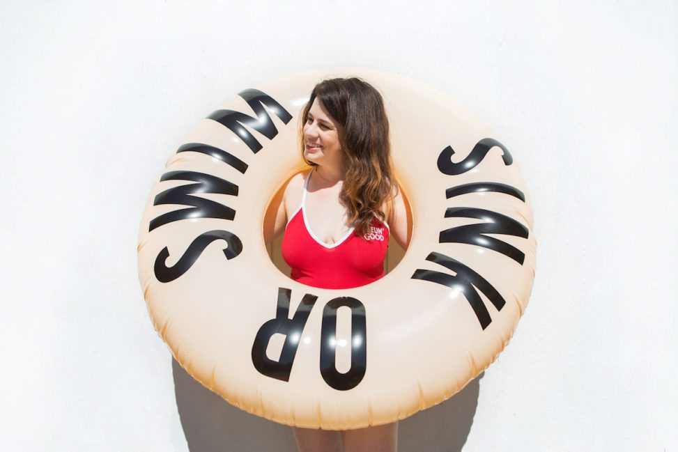 woman in red swimsuit holding an inner tube that reads "Sink or Swim"