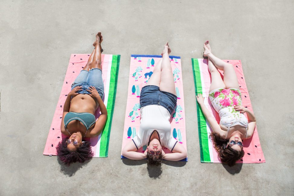 three women laying out on pink beach towels in the sun