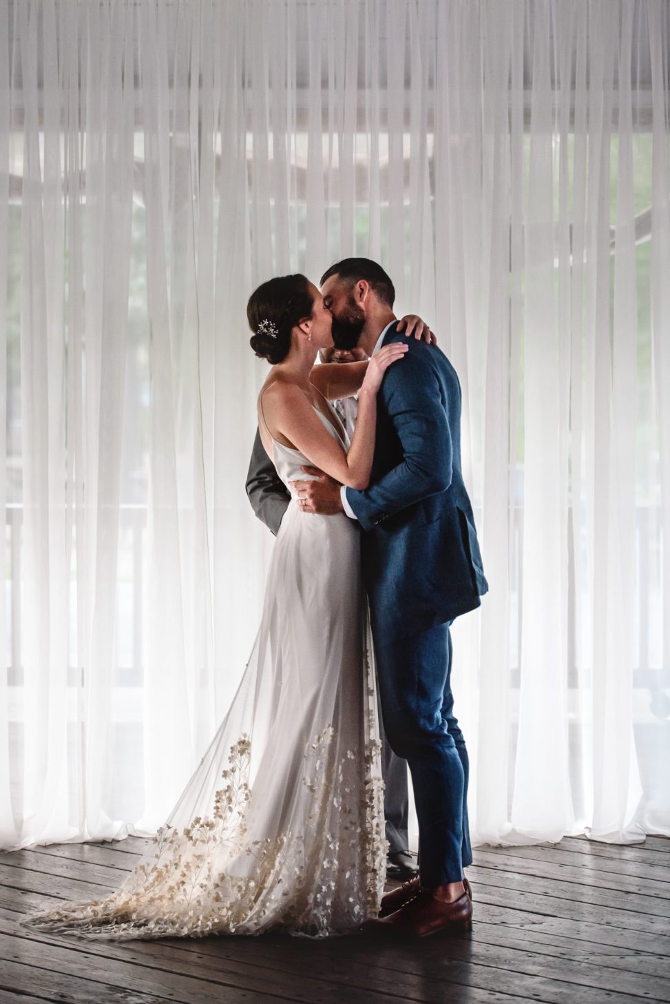bride and groom kissing in front of wall of sheer white drapes