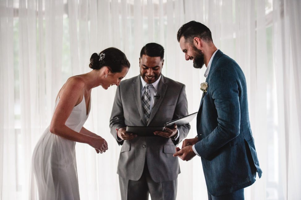 bride and groom standing with officiant during ceremony and laughing